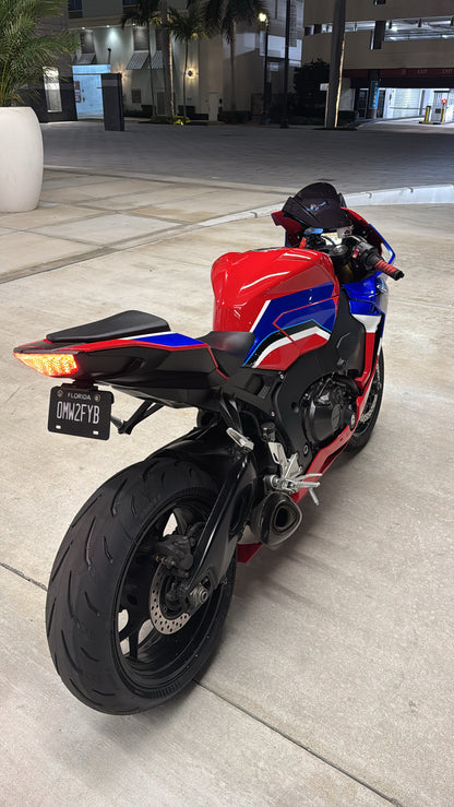 A motorcycle with a red, blue, and white striped fairing, viewed from the rear, with a focus on the license plate area.