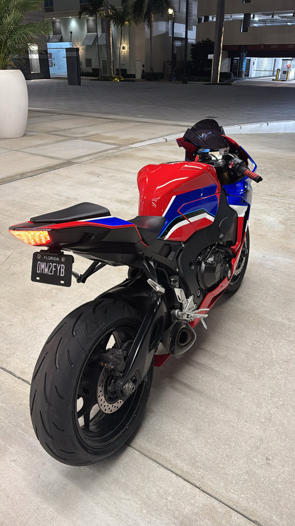 A motorcycle with a red, blue, and white striped fairing, viewed from the rear, with a focus on the license plate area.