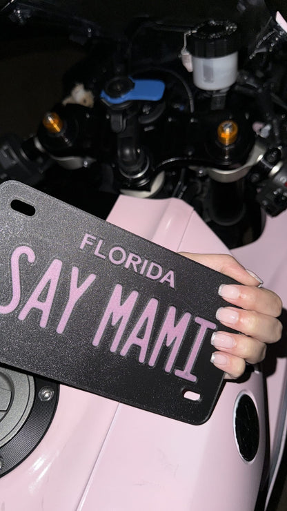 Custom motorcycle vanity plate, pink and black with text "SAY MAMI"